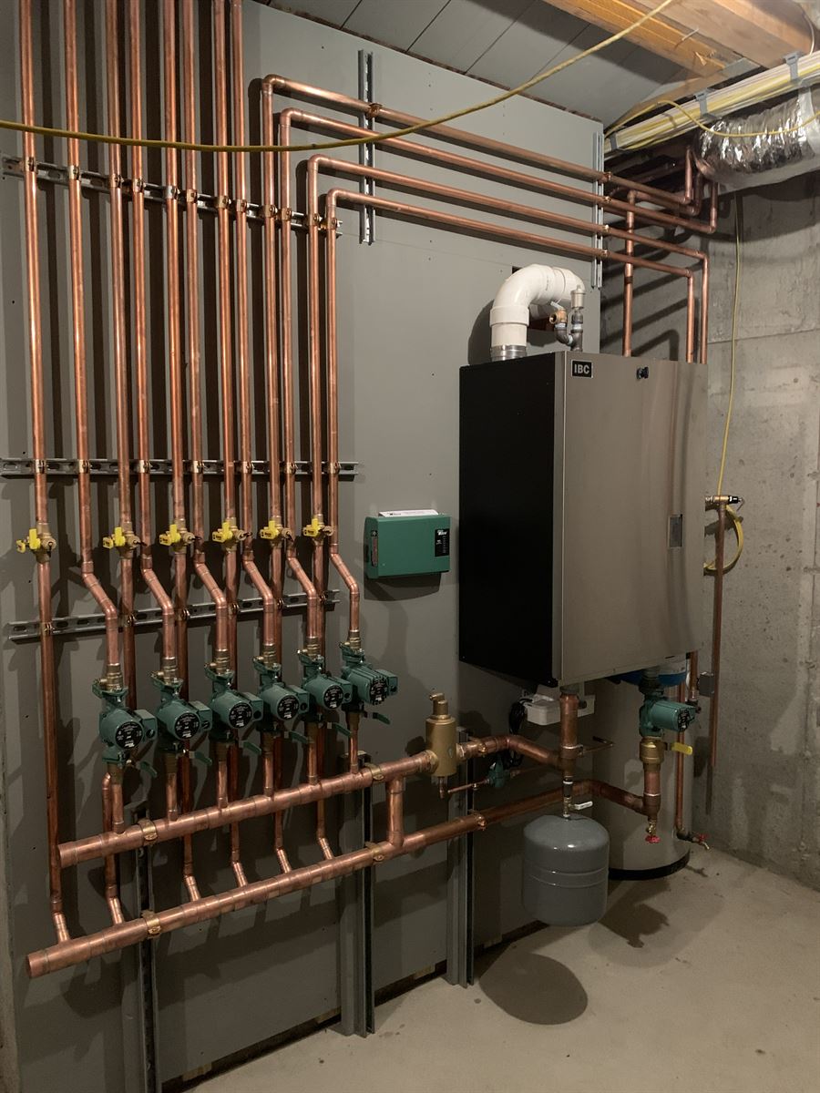 New construction boiler room with an IBC wall-hung boiler, six-zone copper manifold and circulator pumps